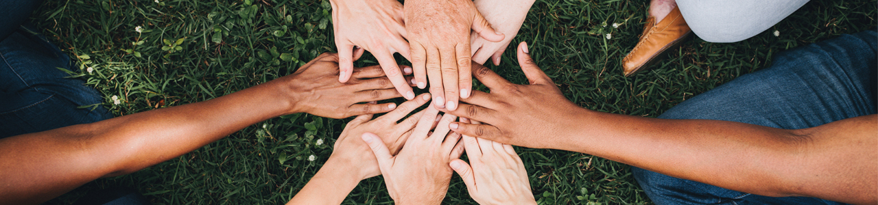 Menschen unterschiedlicher Hautfarben halten ihre Hände übereinander.