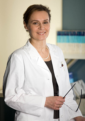 Lächelnde Frau Zahnärztin Eva Dakowitz bekleidet in weißen Kittel steht in Ihrem Büro.