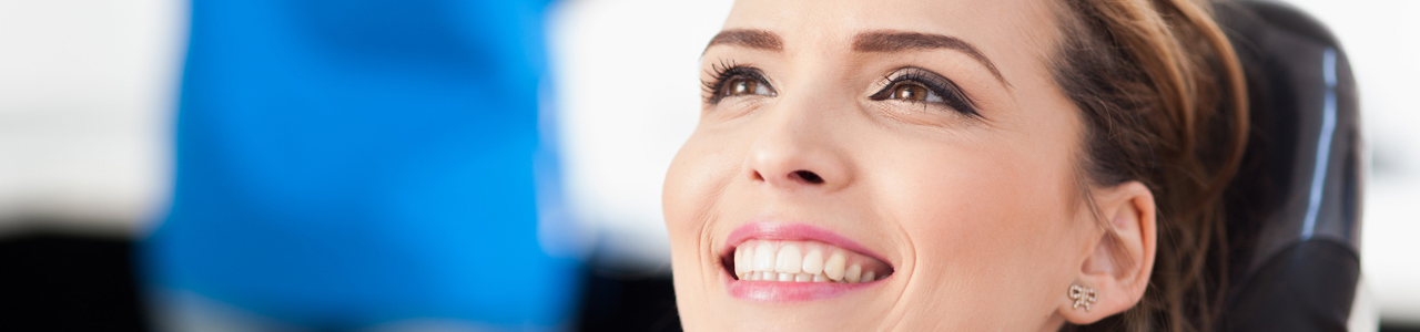 Eine Frau lächelt auf dem Behandlungsstuhl beim Zahnarzt.