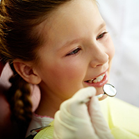 Zahnarzt untersucht Zähne eines kleinen, lächelnden Mädchens