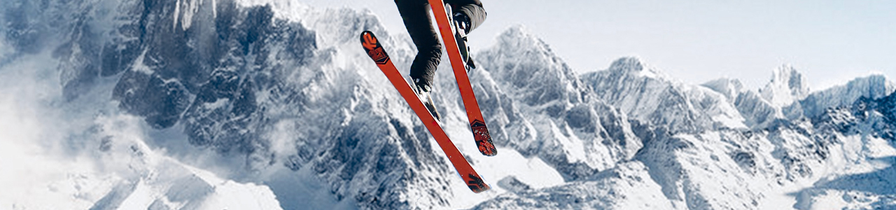 Ein Skifahrer springt gewagt mit seinen Skiern. Im Hintergrund sieht man eine schneebedeckte Berglandschaft.